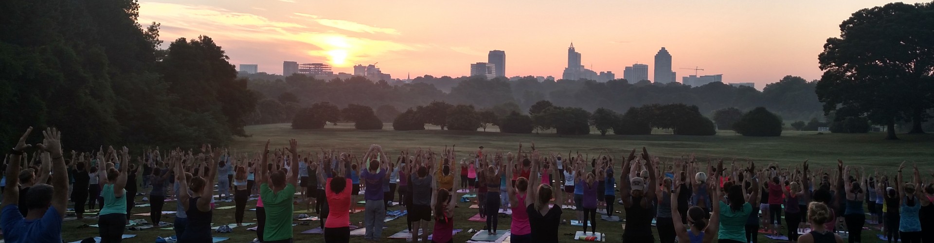 Crowd of people doing yoga in a field at Dix Park with the sun rising in the background
