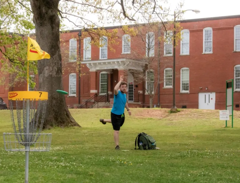 Disc golfer puts into a basket at Dix Park
